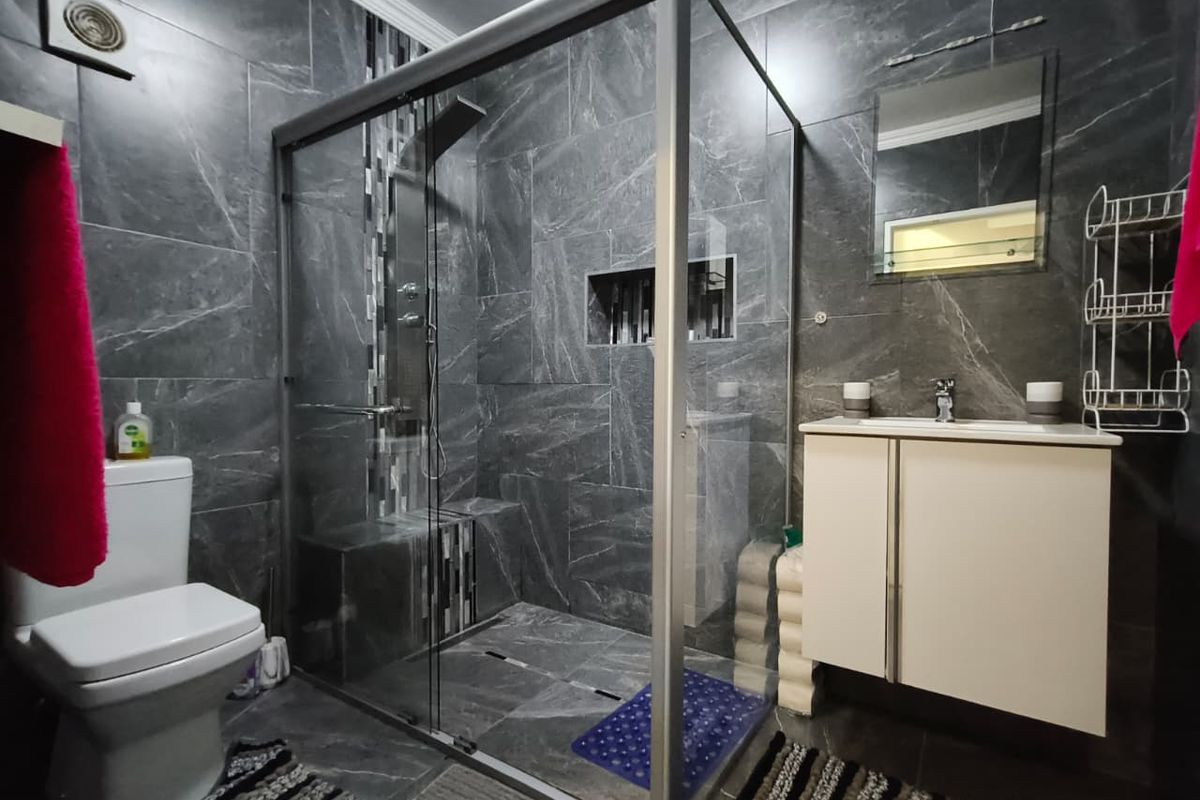Modern bathroom featuring dark marble-effect wall and floor tiles, a glass-enclosed walk-in shower with built-in bench, and a wall-mounted vanity unit.