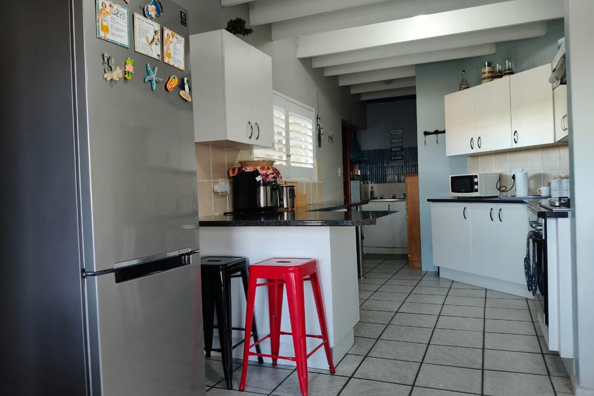 A functional kitchen featuring white cabinetry, dark countertops, tiled flooring, and exposed ceiling beams, with an adjacent scullery area visible.