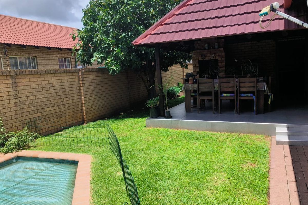 A private backyard featuring a covered patio area, a swimming pool with a safety fence, and a well-maintained lawn.