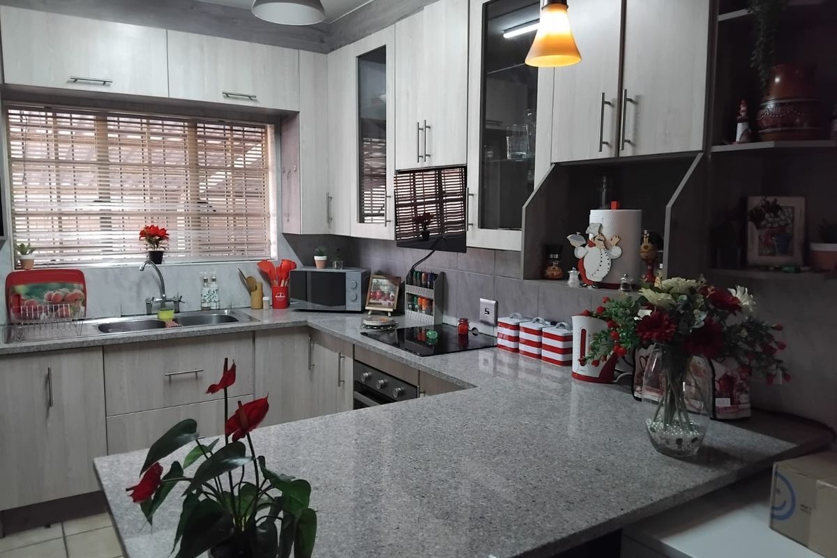 A functional kitchen featuring light wood-grain cabinetry, granite countertops, a double sink, and a built-in electric hob and oven.