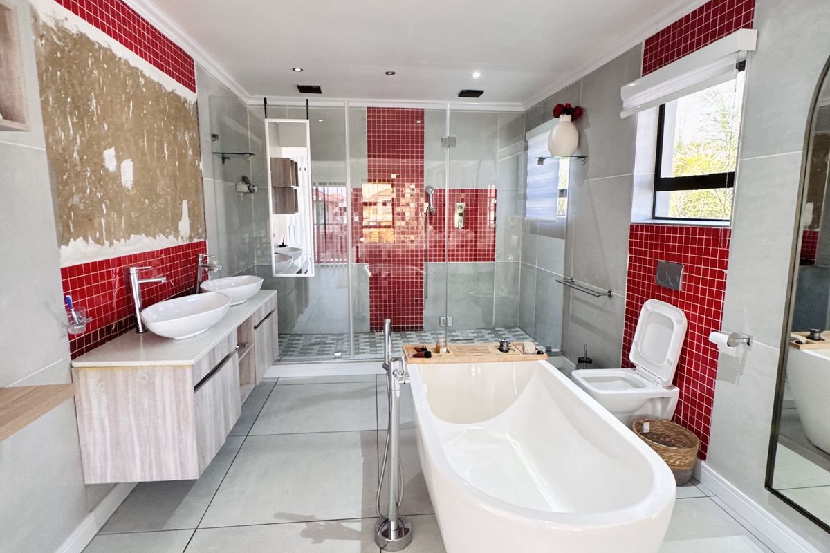 Modern bathroom featuring a freestanding bathtub, double vanity, and a glass-enclosed walk-in shower with red mosaic tile accents.