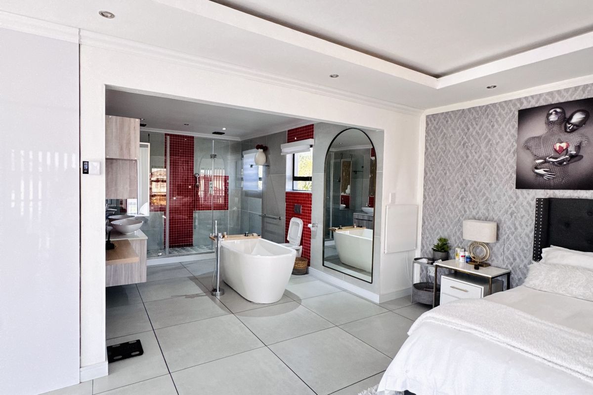 Spacious open-plan bedroom featuring an integrated en-suite bathroom with a freestanding bathtub, glass-enclosed shower, and modern tiled finishes.