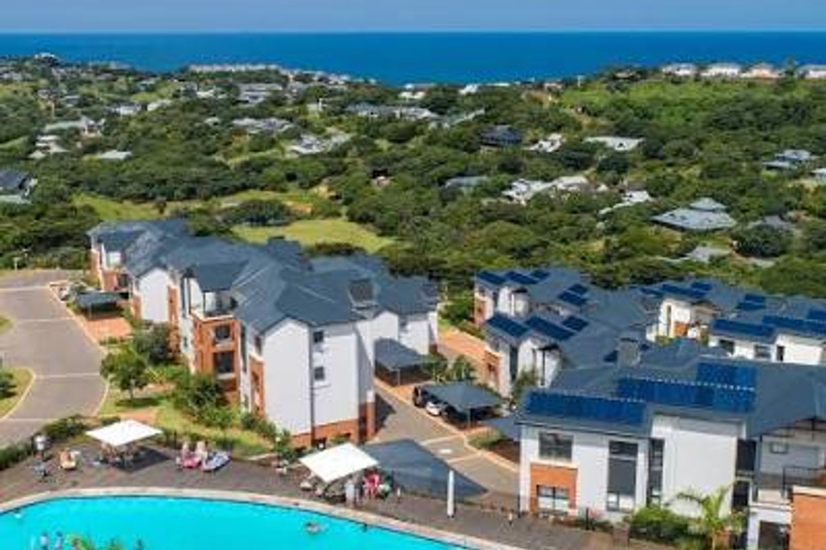 Aerial view of a residential apartment complex featuring a large swimming pool, landscaped grounds, and coastal views.