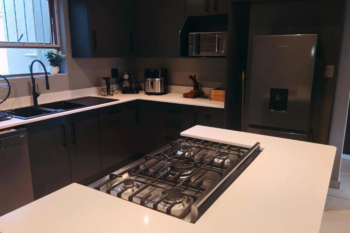 Modern kitchen featuring dark cabinetry, white stone countertops, a central island with a built-in gas hob, and integrated appliances.