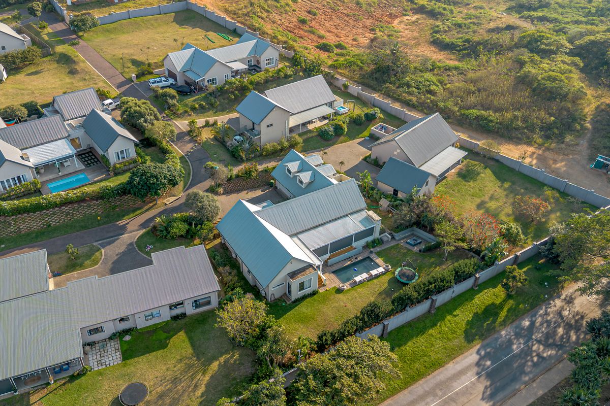 Aerial view of a residential estate featuring multiple detached houses with metal roofs, landscaped gardens, and private swimming pools.