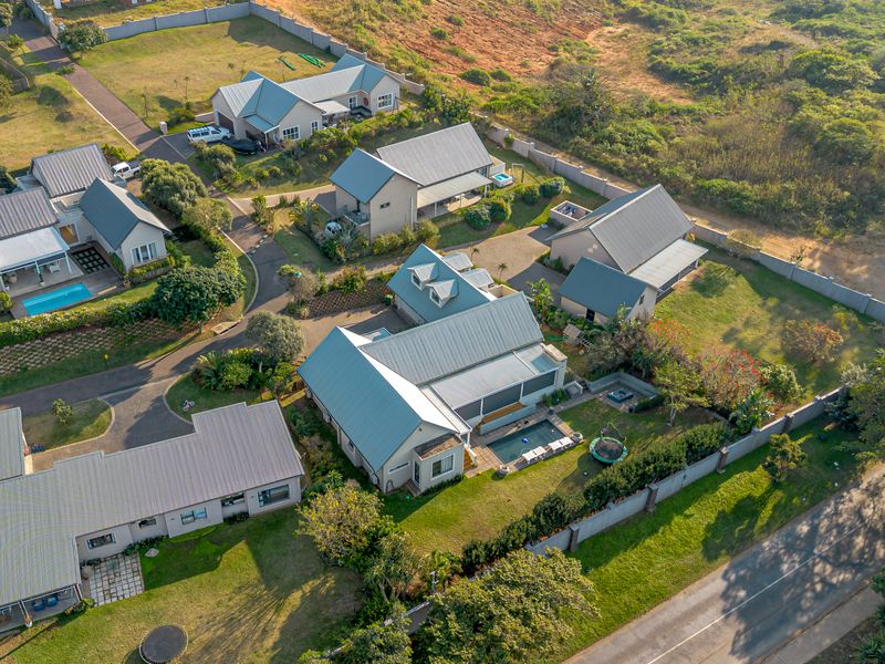 Aerial view of a residential estate featuring multiple detached houses with metal roofs, landscaped gardens, and private swimming pools.