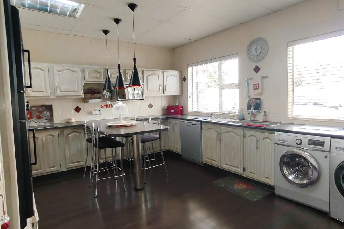 Spacious kitchen featuring traditional cabinetry, integrated laundry appliances, dark wood-look flooring, and a central breakfast bar with pendant lighting.