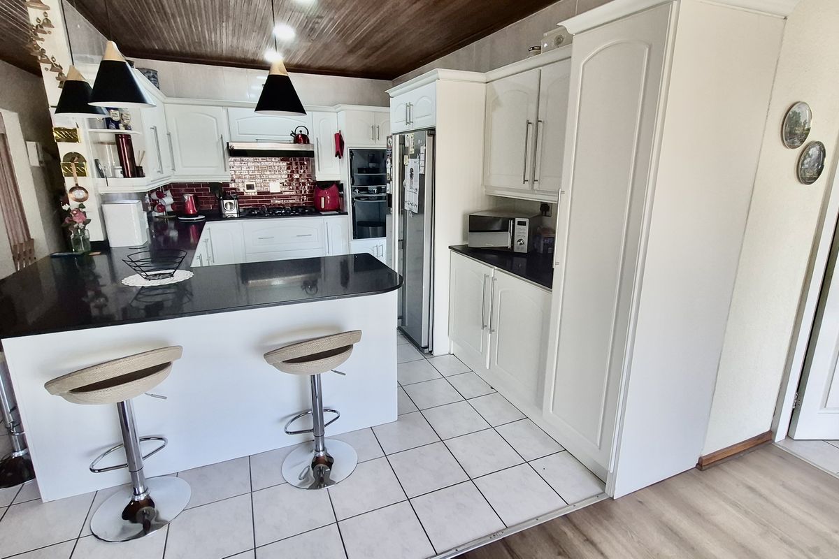 A functional kitchen featuring white cabinetry, dark granite countertops, a breakfast bar, built-in oven, and a tiled backsplash.