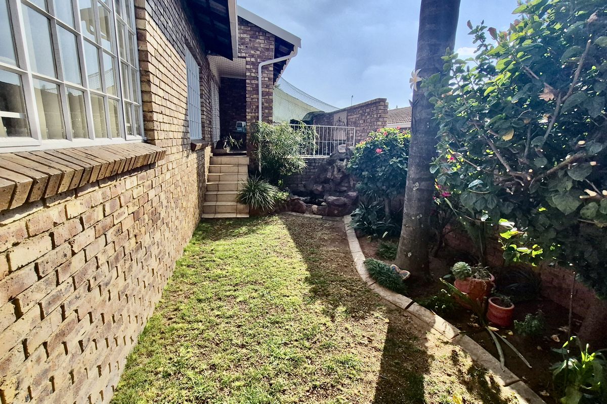 A side garden area featuring a brick exterior wall, a small set of stairs leading to an entrance, and established garden landscaping.