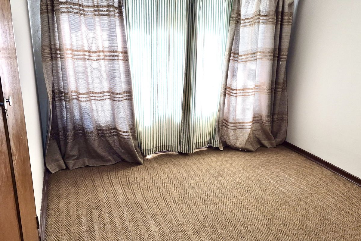 A simple bedroom featuring carpet flooring and a wooden door, providing a neutral space ready for personalization.