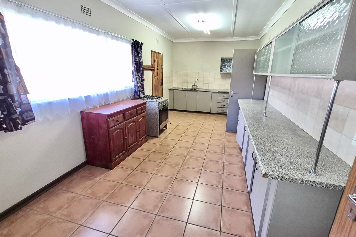 A functional kitchen featuring tiled flooring, built-in cabinetry, a stainless steel sink, and a freestanding stove, offering a practical layout for daily meal preparation.
