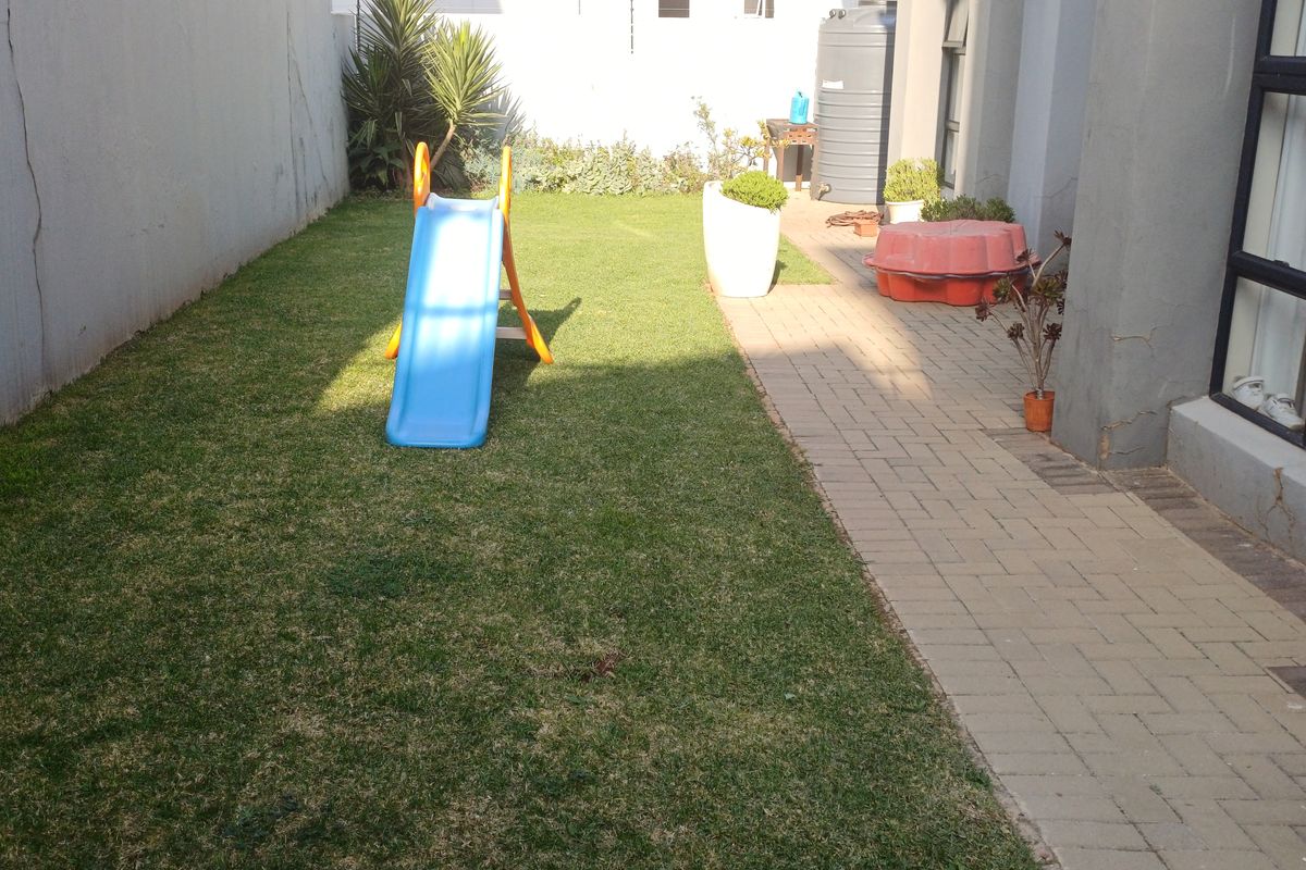 A rear garden area featuring a paved walkway, a small lawn, and a water storage tank, with visible wear to the boundary wall plaster.
