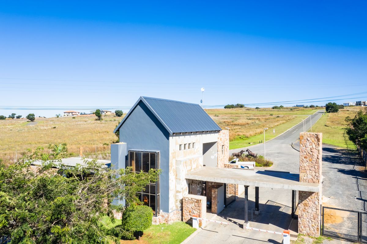 Aerial view of a residential estate entrance gatehouse featuring stone cladding, modern architectural design, and paved access road.