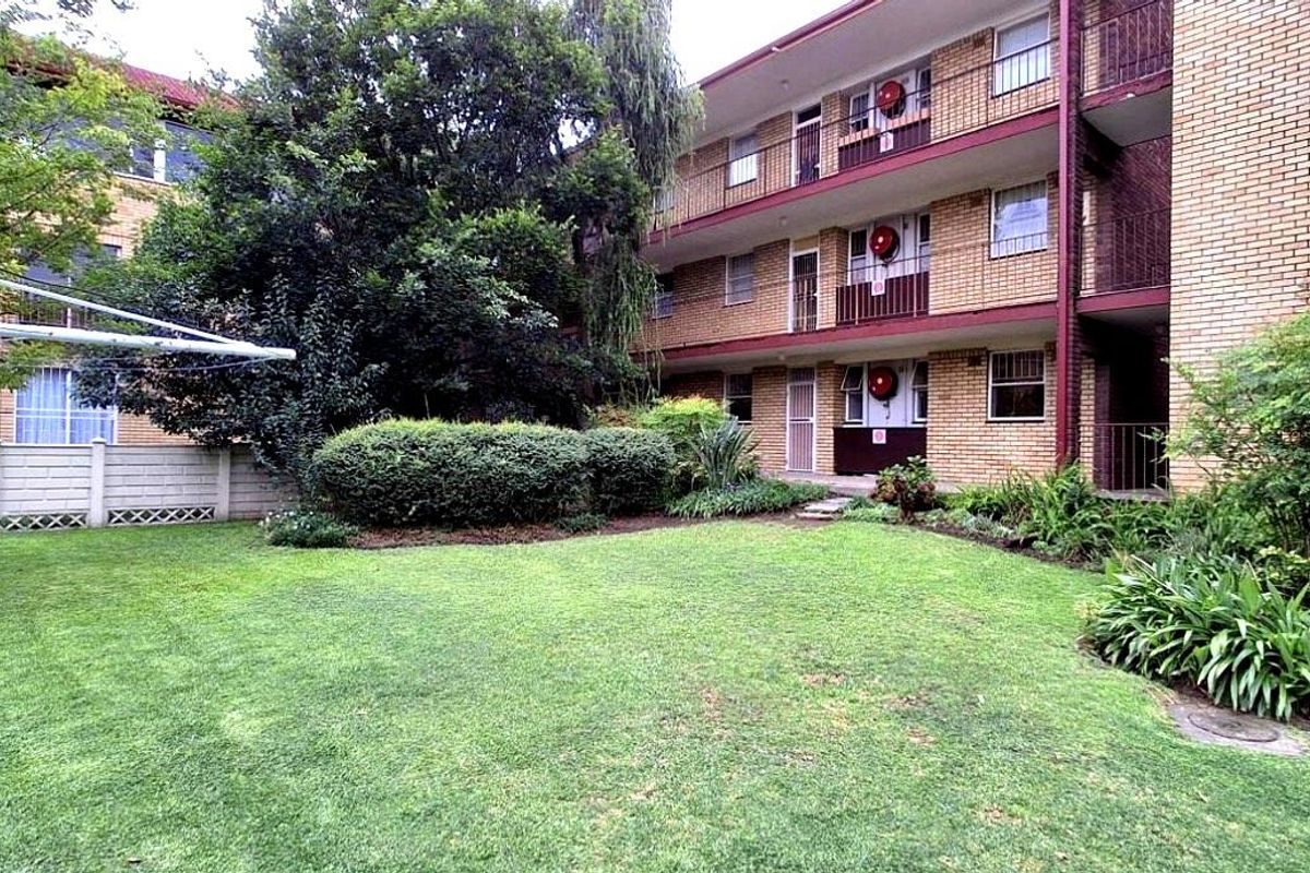 A view of the apartment complex rear facade featuring a shared garden area with established landscaping and multi-level balconies.