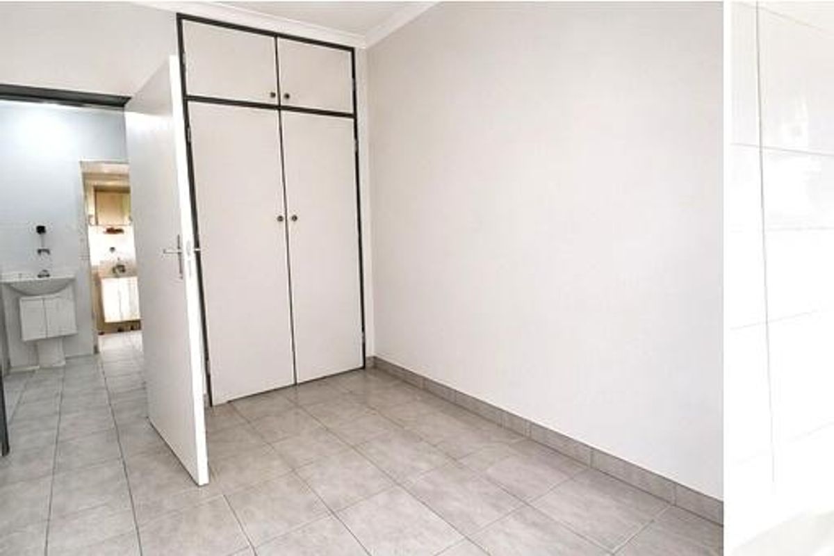 A bedroom featuring built-in cupboards and tiled flooring, with an adjacent view into a bathroom area.
