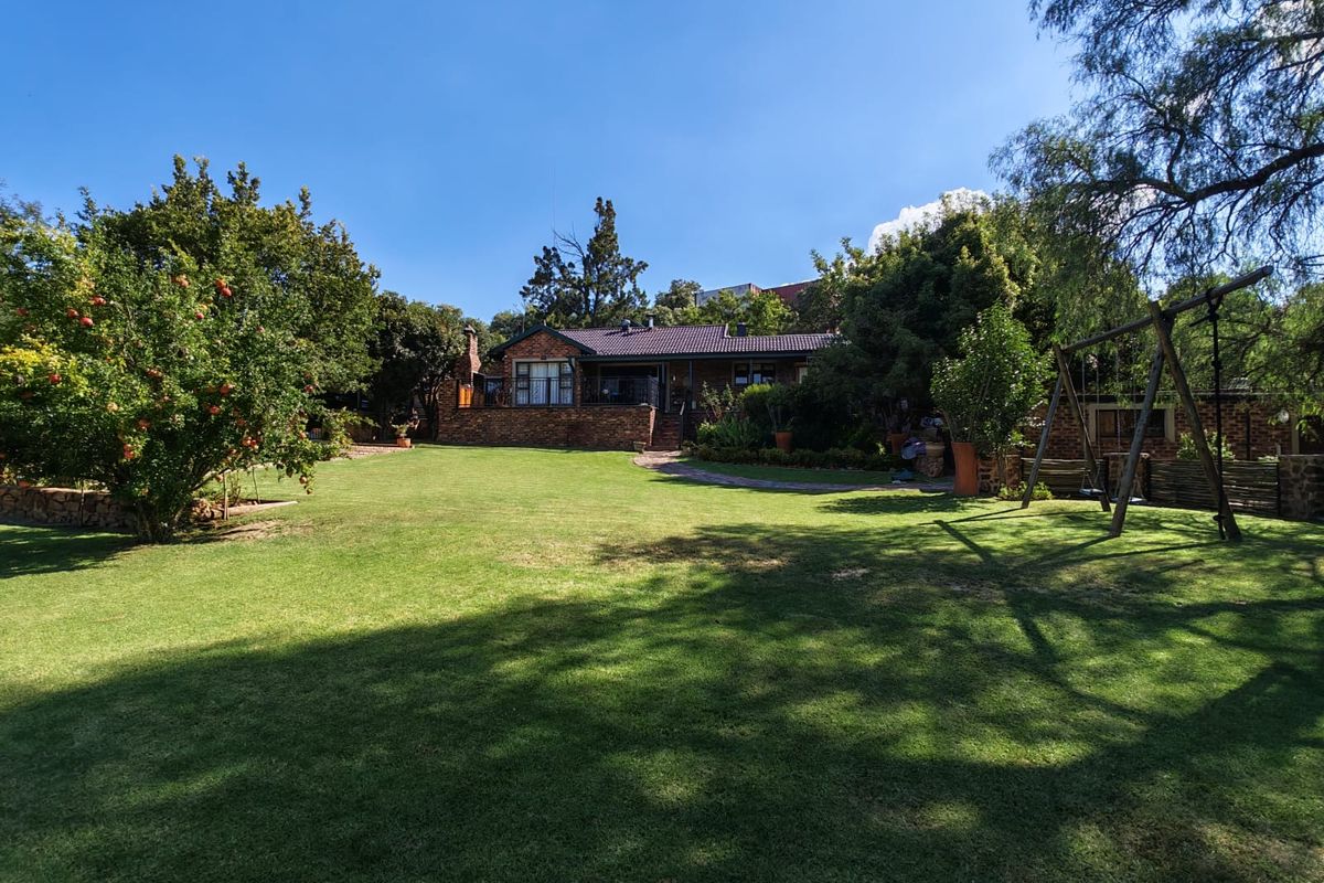 A spacious rear garden featuring a well-maintained lawn, mature trees, and a view of the brick-built house with a covered patio area.