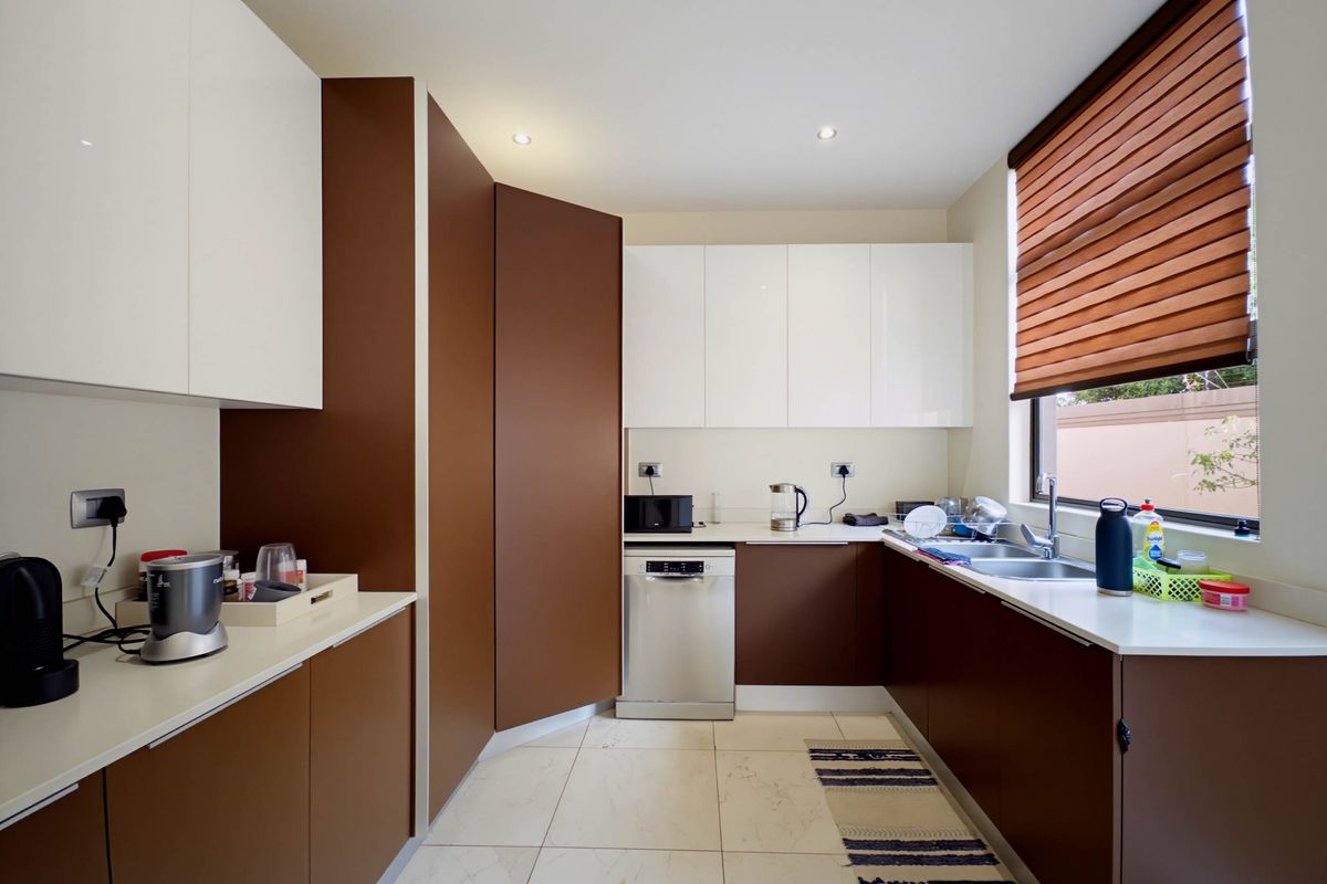 Modern kitchen featuring two-tone brown and white cabinetry, stone countertops, integrated dishwasher, and a double sink with a window view.