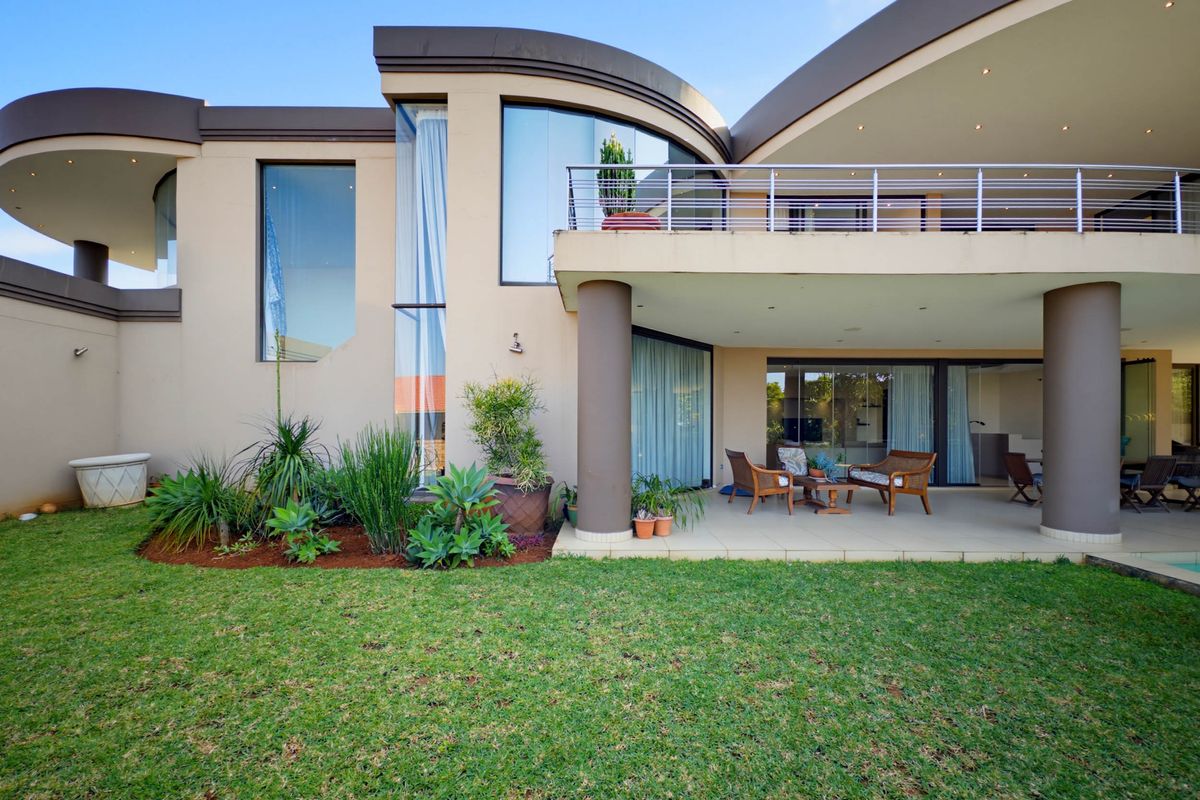 Rear view of a modern architectural home featuring a covered patio, upper-level balcony with stainless steel balustrades, and a well-maintained garden.