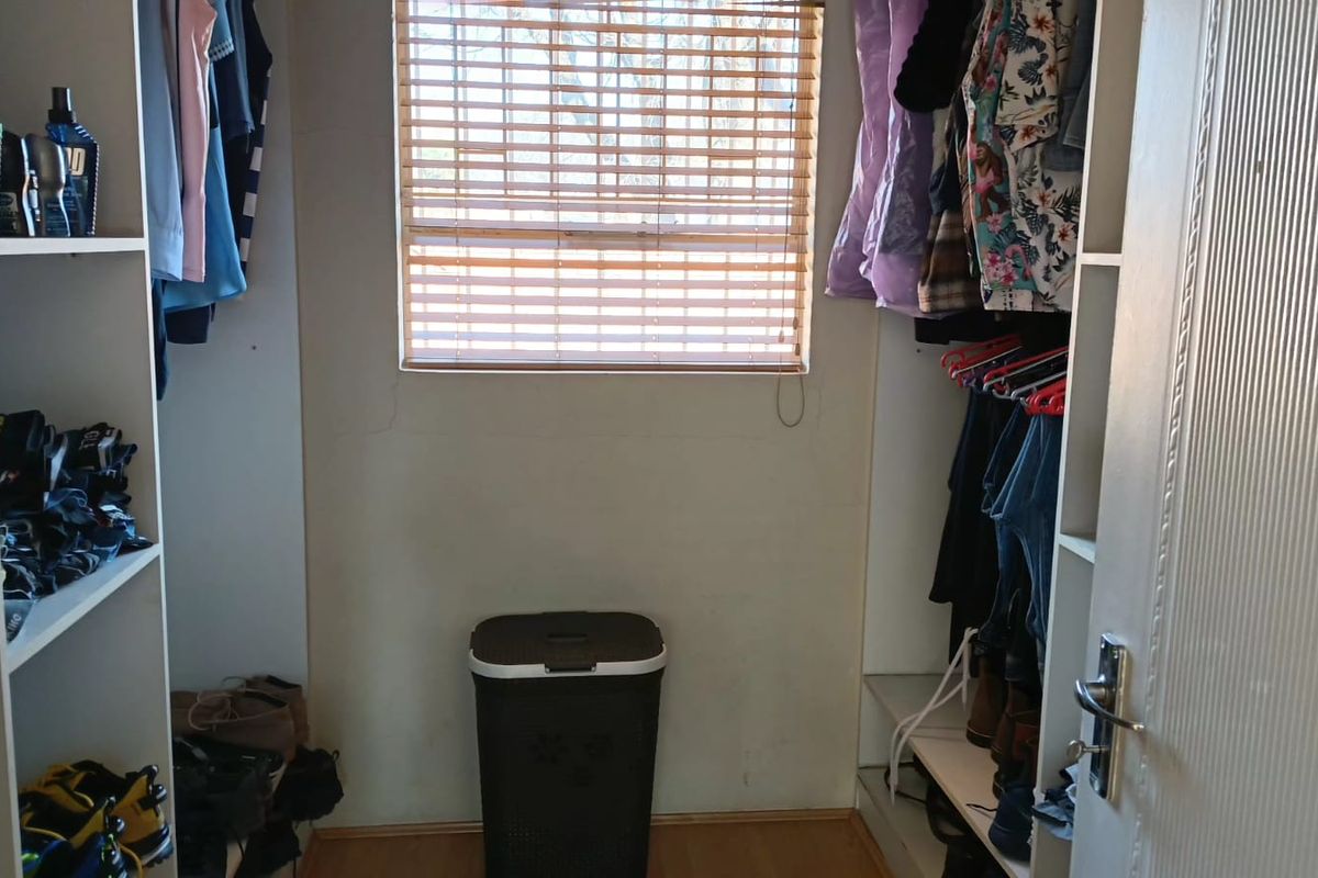 A walk-in closet or dressing area featuring built-in shelving units, laminate flooring, and a window with fitted venetian blinds.