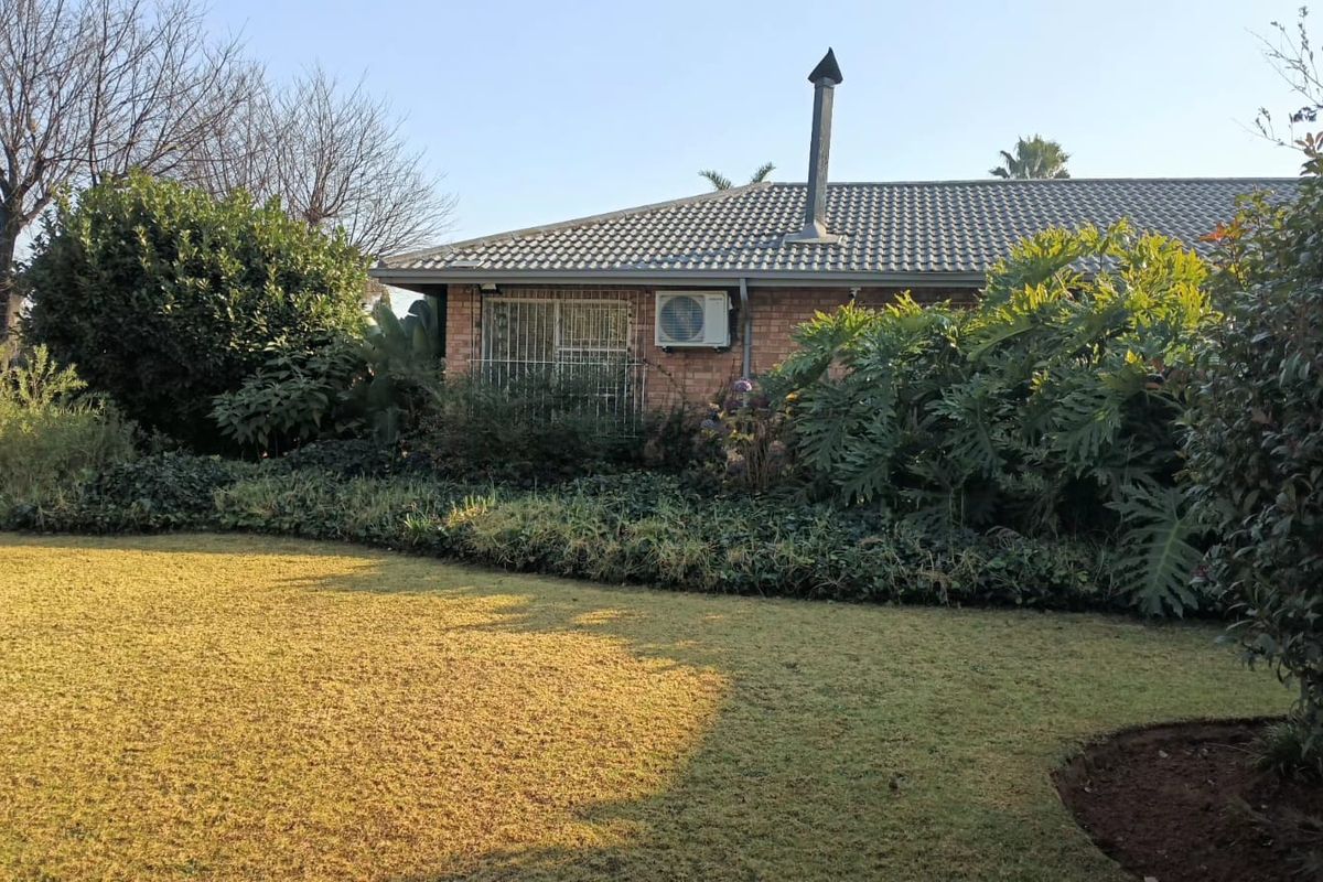 Rear view of a brick house featuring a tiled roof, chimney, and established garden with a lawn area.