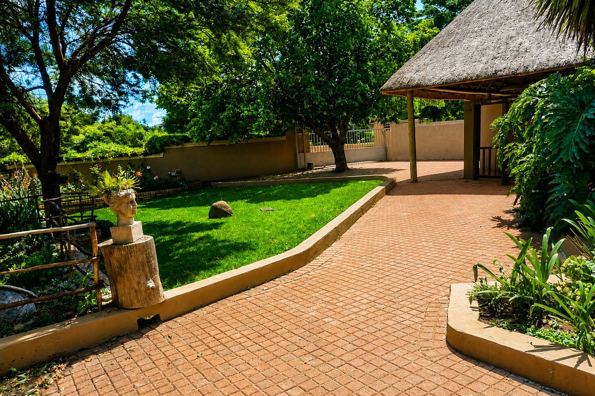 A well-maintained rear garden featuring a paved walkway, lush lawn, mature trees, and a covered thatched-roof patio area.