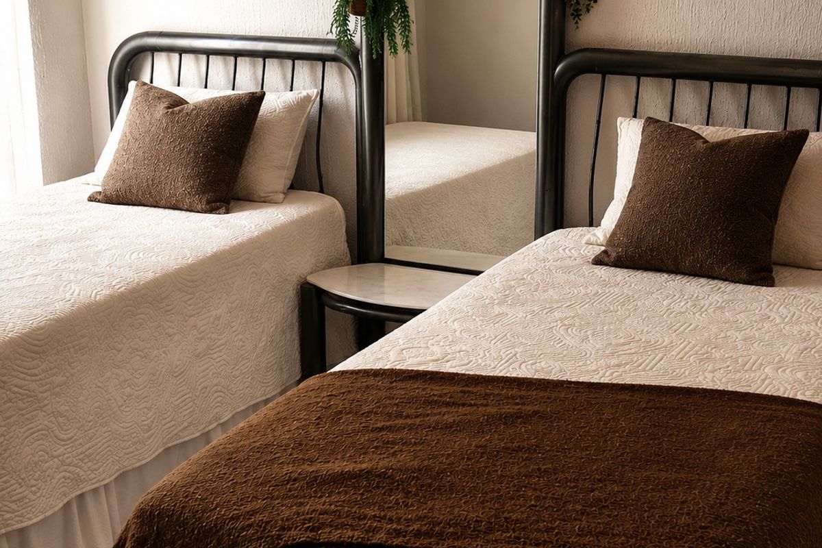 A well-maintained bedroom featuring neutral textured walls and carpeted flooring, comfortably accommodating two twin beds.