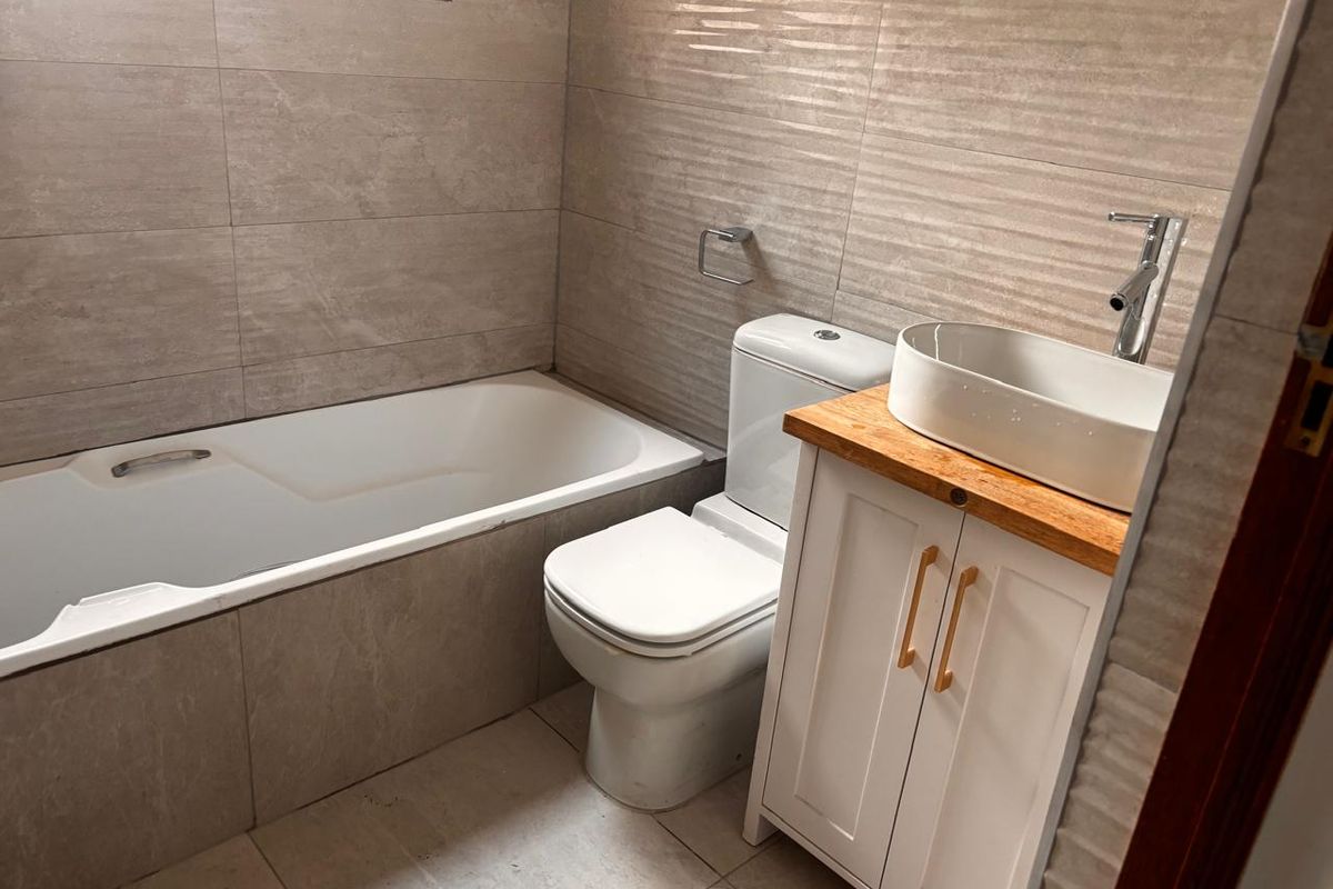 A modern bathroom featuring a bathtub, a white vanity cabinet with a vessel sink, and neutral-toned wall and floor tiles.