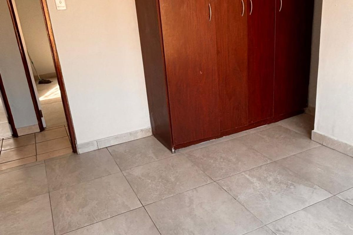 A vacant bedroom featuring neutral tiled flooring and a large, dark wood-finish built-in wardrobe, offering a clean and functional space.