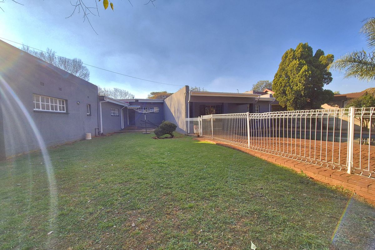 A spacious rear garden featuring a lawn area, a fenced swimming pool, and direct access to the main house structure.
