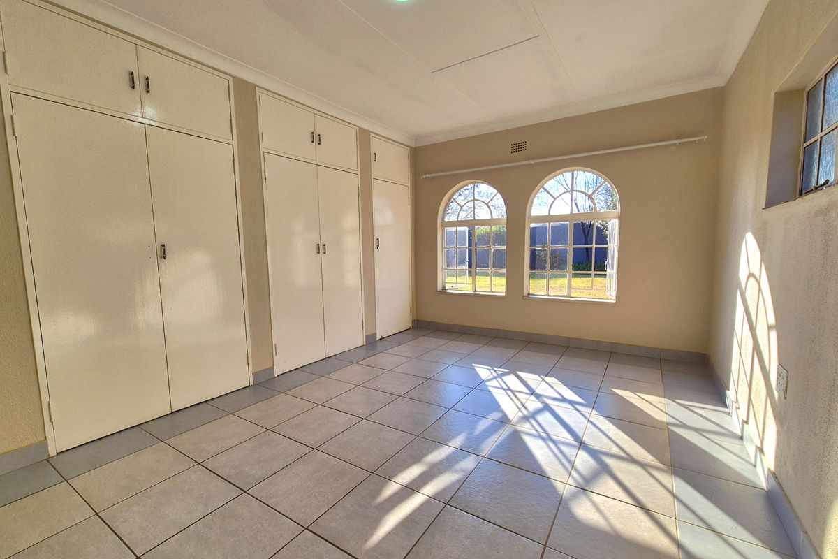 A bright, empty bedroom featuring built-in floor-to-ceiling cupboards, tiled flooring, and distinctive arched windows allowing for ample natural light.