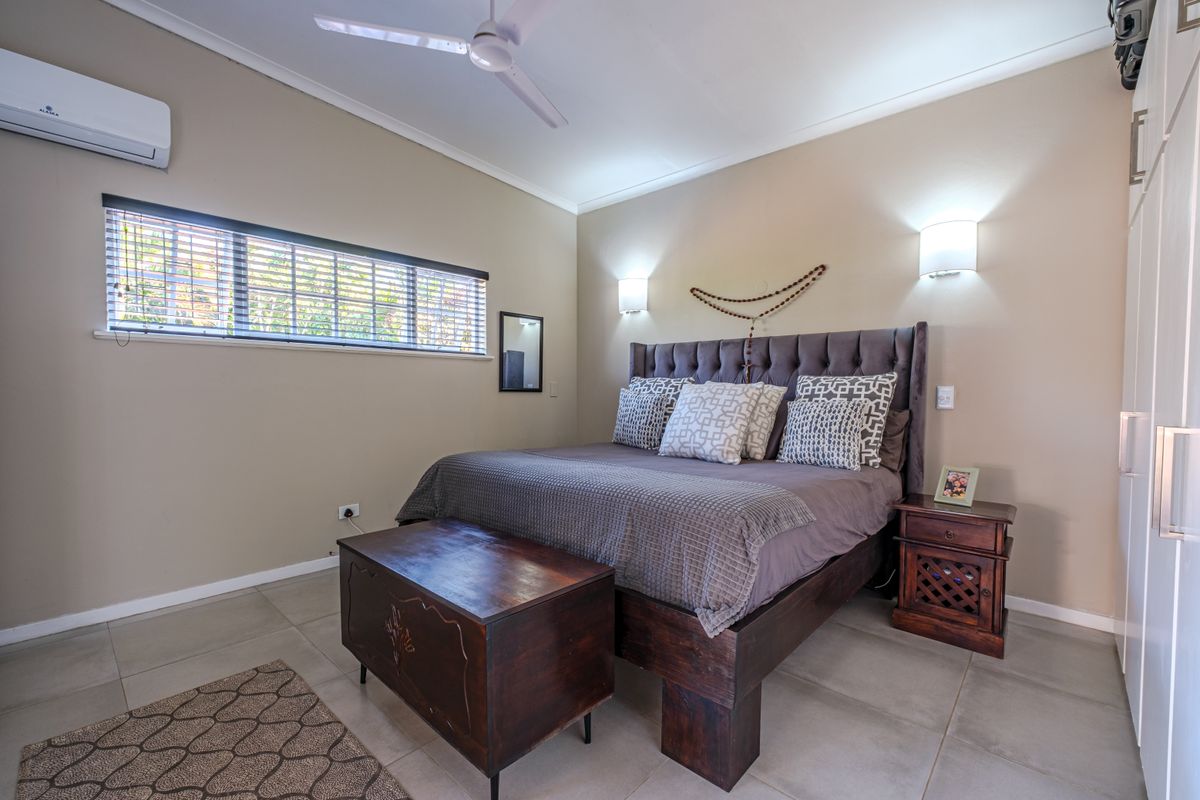 A well-maintained bedroom featuring tiled flooring, a ceiling fan, wall-mounted air conditioning unit, and built-in cupboards.