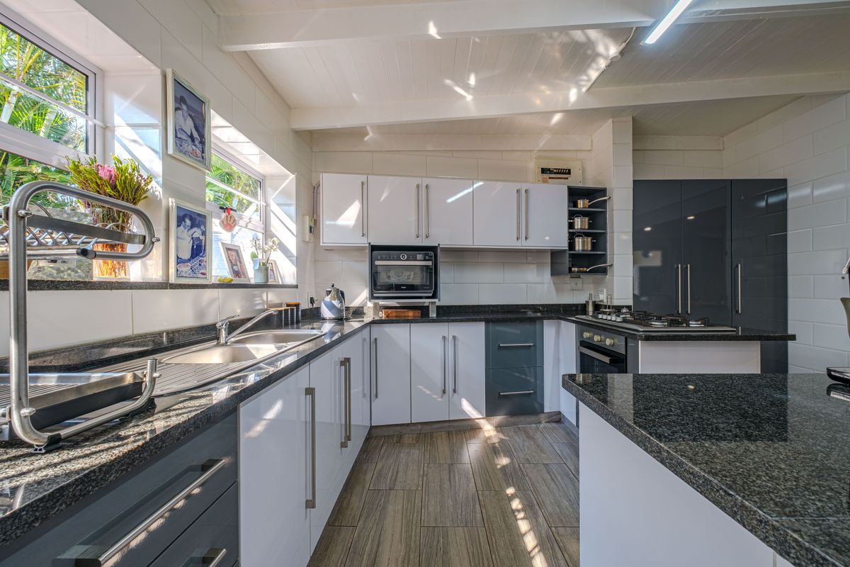 Modern kitchen featuring granite countertops, high-gloss cabinetry, built-in oven, gas hob, and tiled flooring with ample natural light.