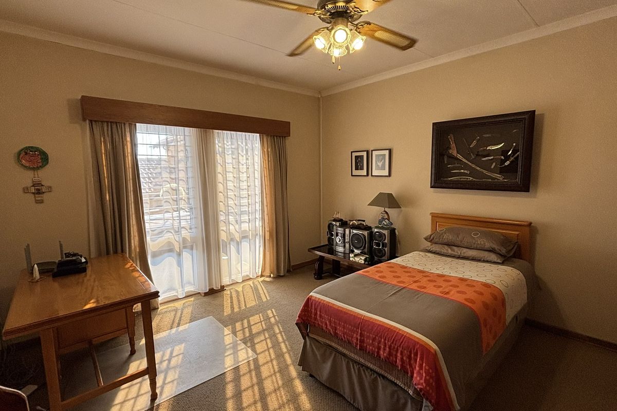 A functional bedroom featuring carpeted flooring, a ceiling fan, and a sliding glass door providing natural light.