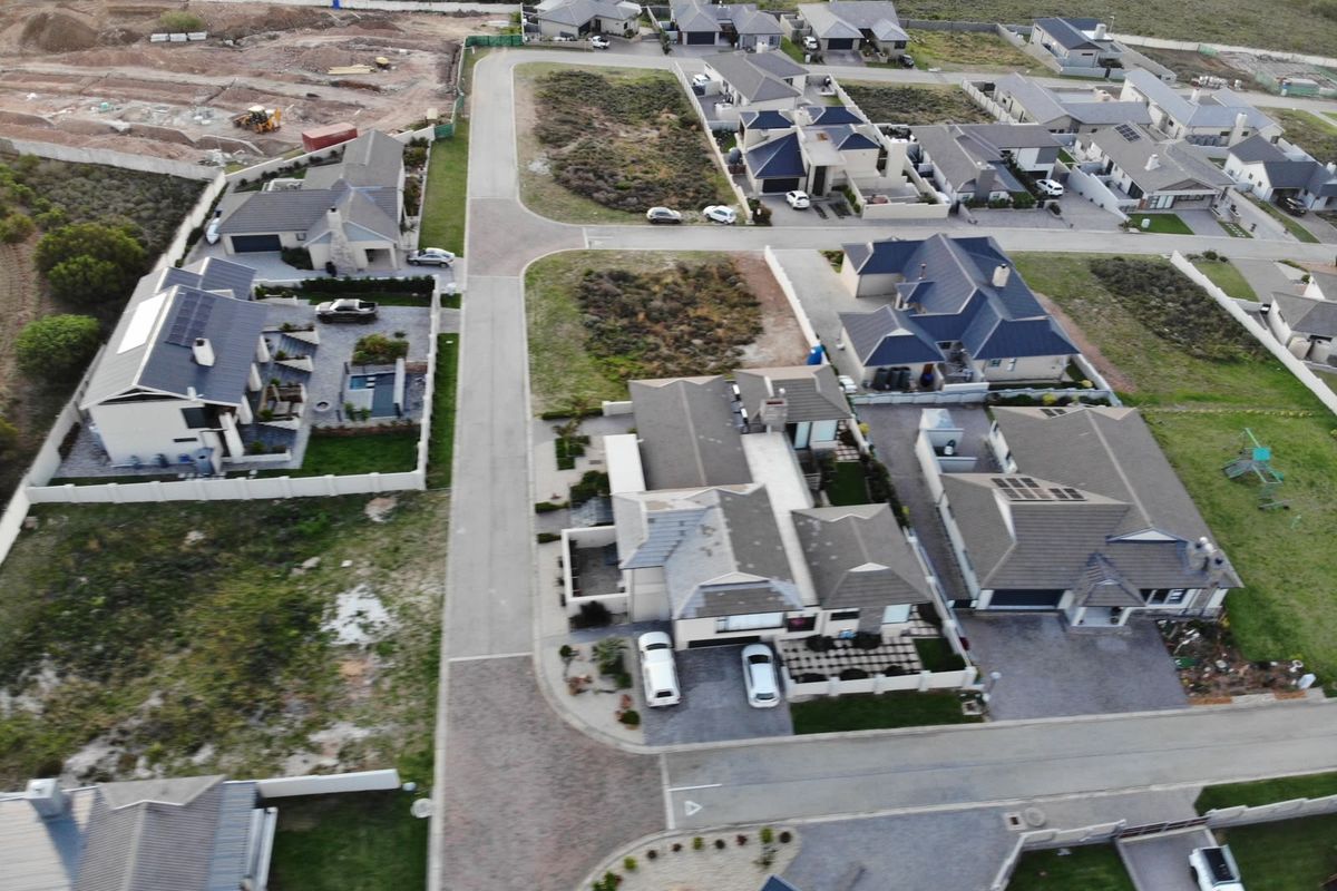 An aerial view of a residential estate featuring paved roads, established housing, and surrounding vacant land plots.