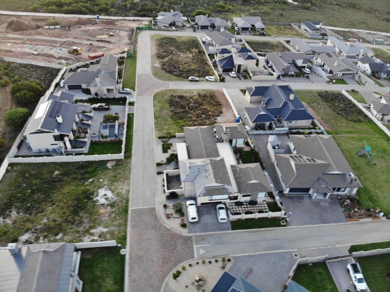 An aerial view of a residential estate featuring paved roads, established housing, and surrounding vacant land plots.