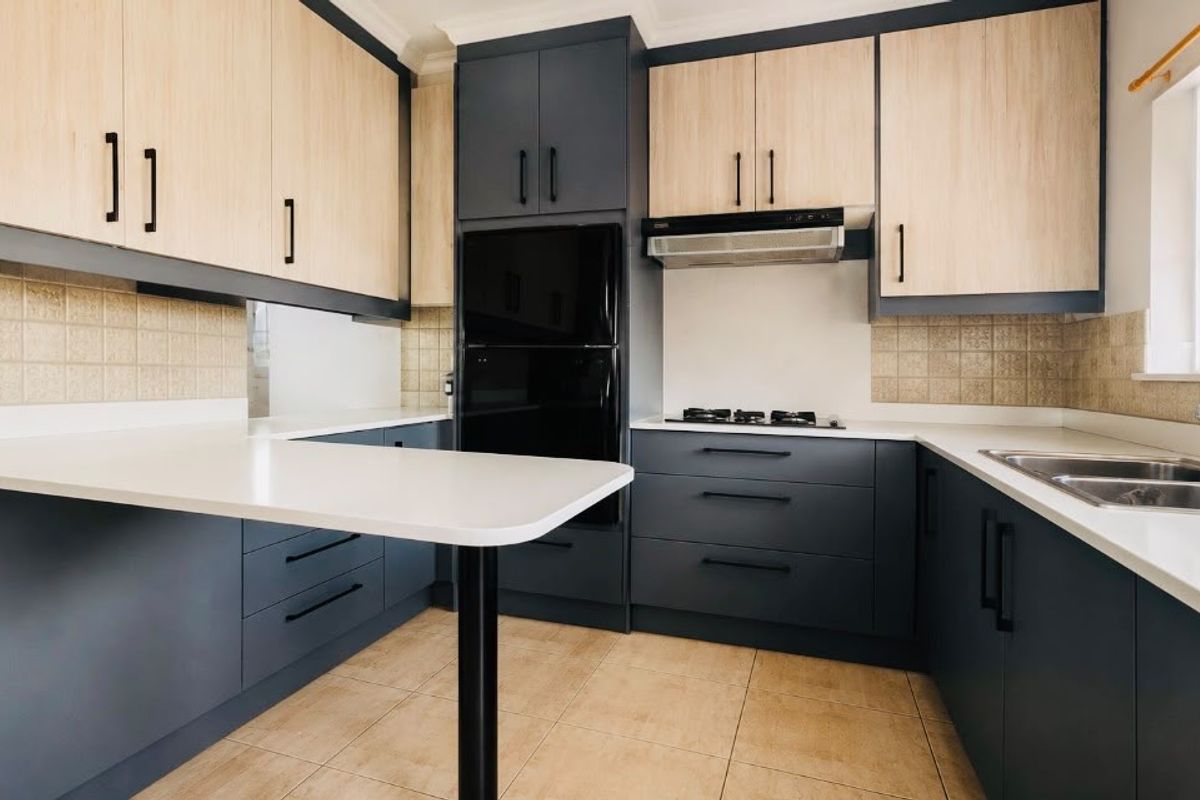 Modern kitchen featuring two-tone cabinetry, stone countertops, built-in gas hob, extractor fan, and a double sink with a breakfast nook extension.