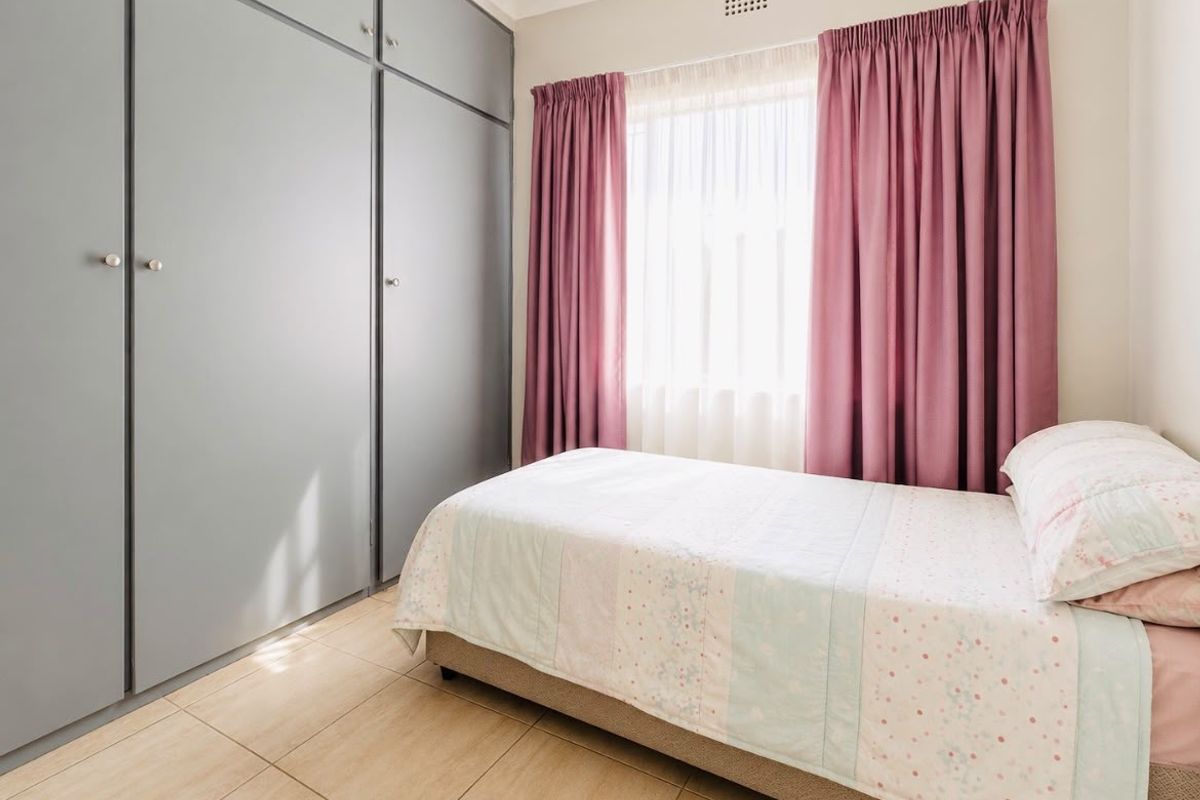 A bedroom featuring built-in floor-to-ceiling grey cabinetry, tiled flooring, and a window with curtain treatments.