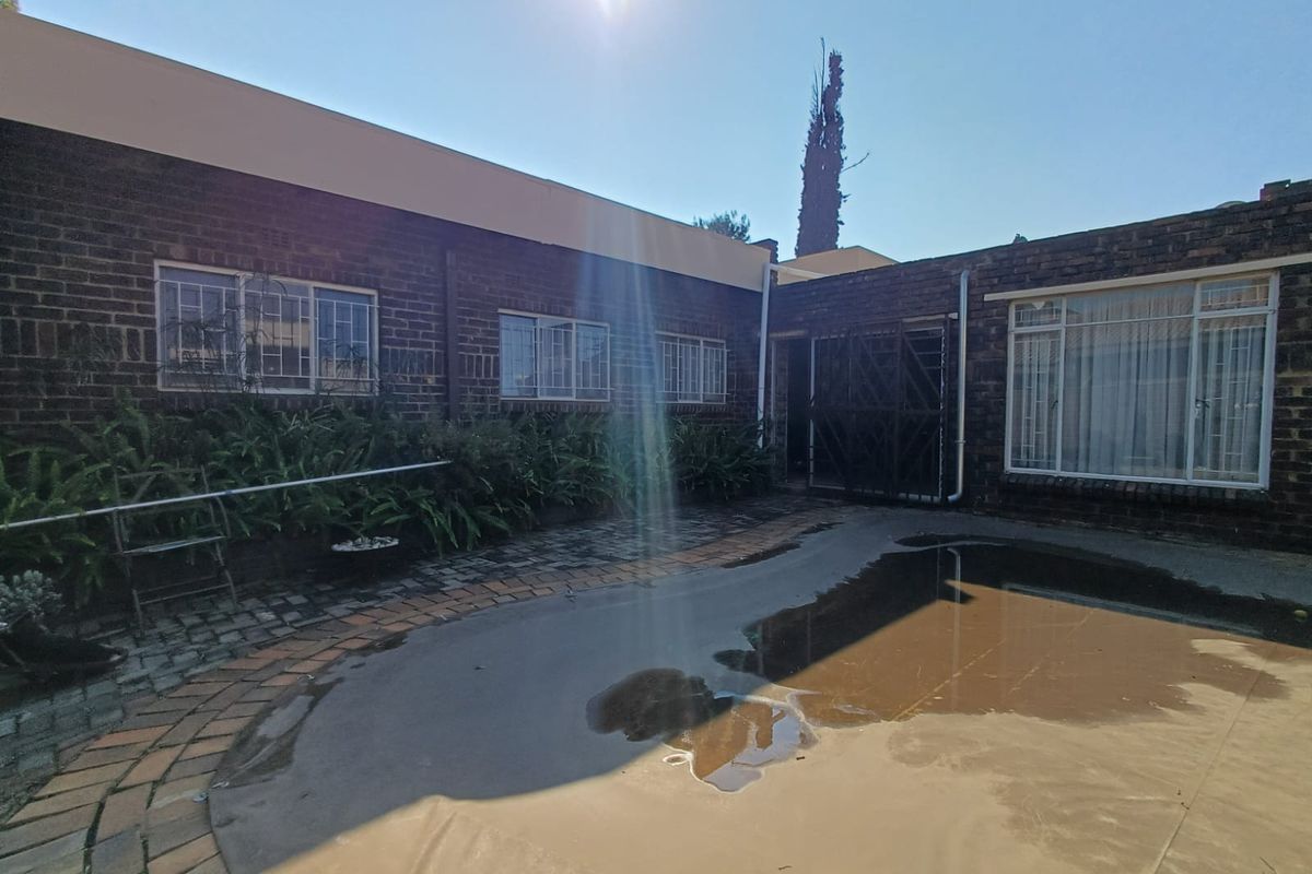 Rear exterior view of the property featuring a brick facade, paved courtyard area, and a swimming pool with a cover.