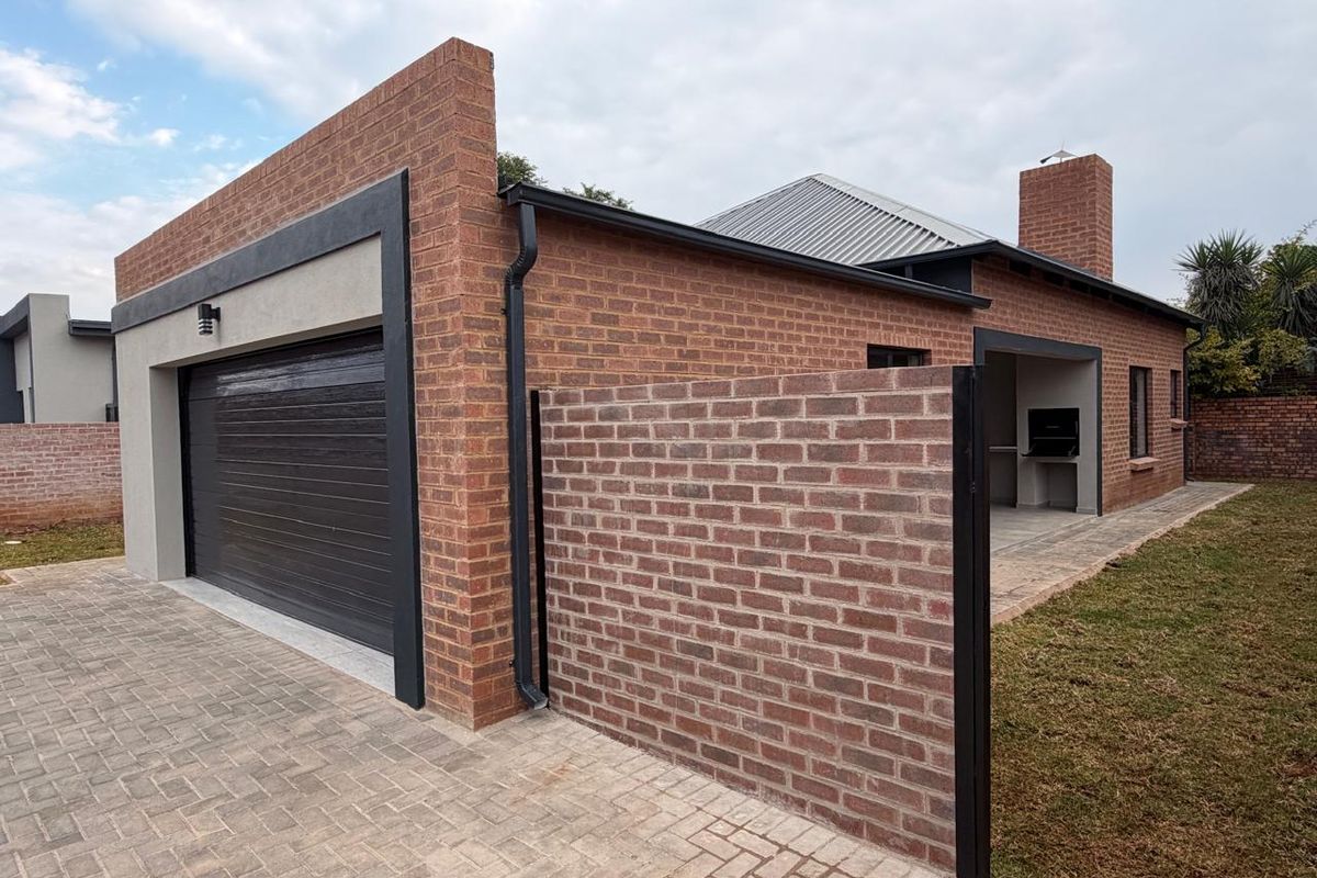 Exterior view of a modern brick house featuring a double garage, paved driveway, and a covered patio area with a built-in braai.