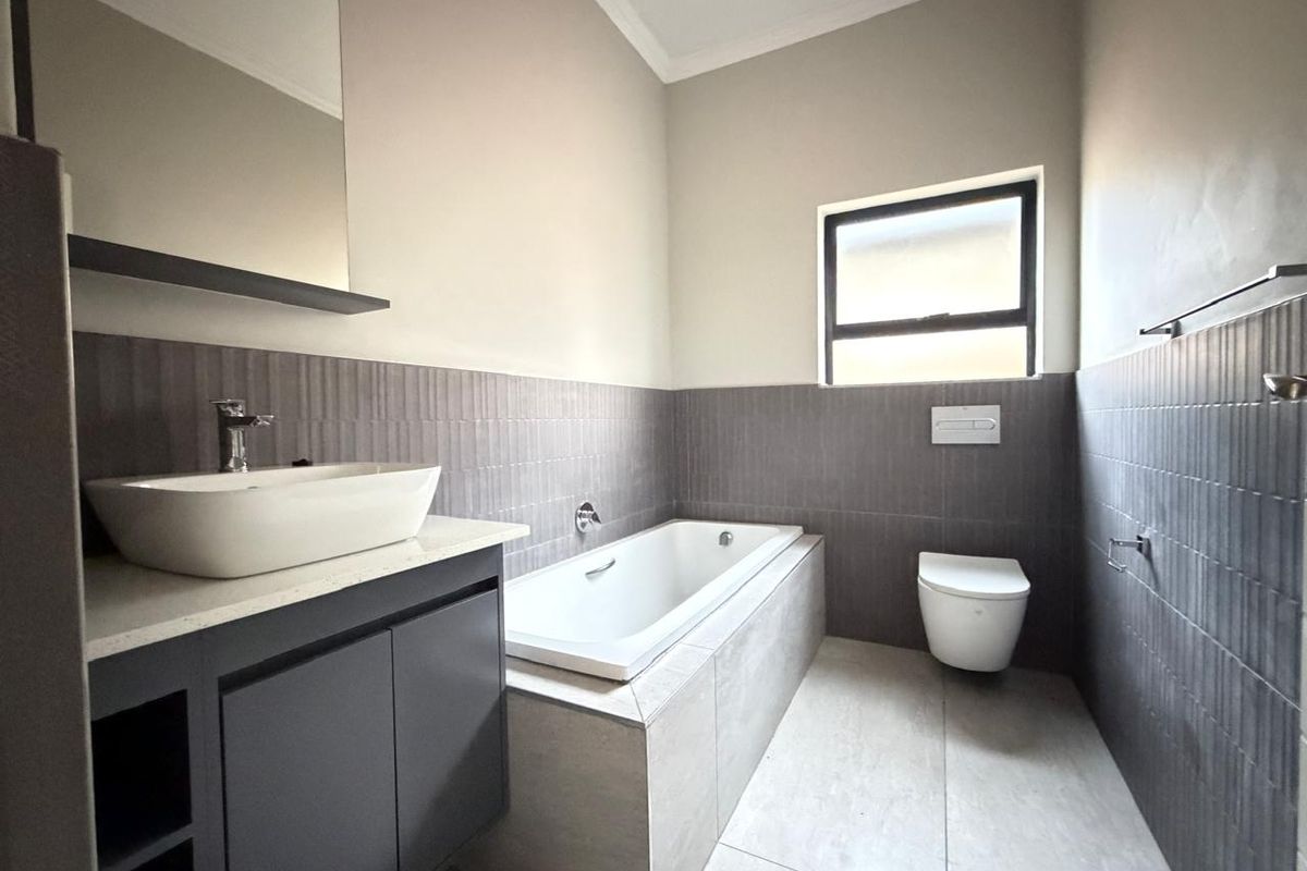 Modern bathroom featuring a built-in bathtub, wall-mounted toilet, and a vanity with a vessel sink and mirror.