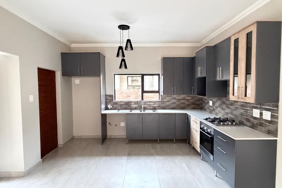 Modern kitchen featuring dark grey cabinetry, light stone countertops, a built-in oven, gas hob, and tiled flooring with a neutral color palette.