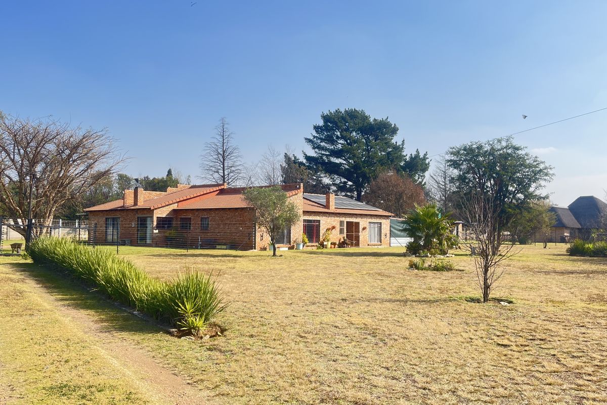 A wide-angle view of a single-story face-brick small holding residence featuring a tiled roof, set within a spacious, established garden landscape.