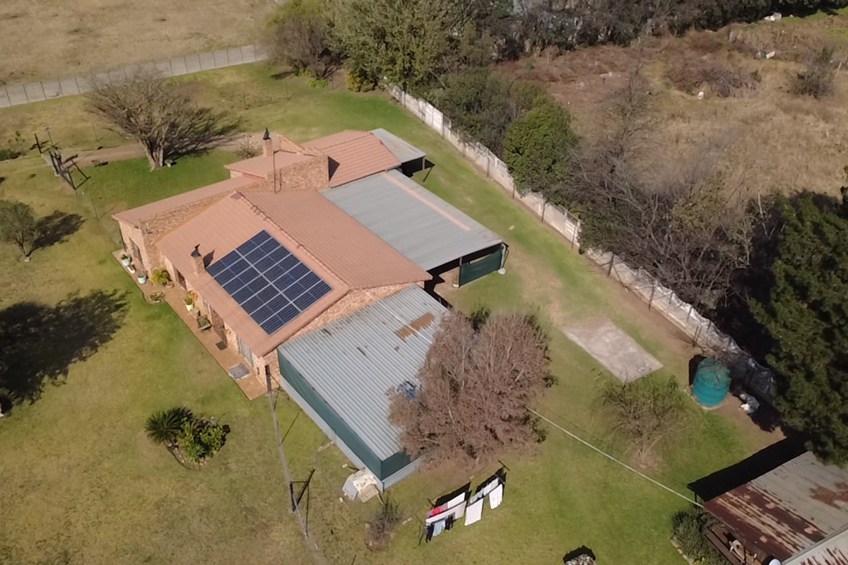 Aerial view of a small holding property featuring a main dwelling with solar panels, a corrugated metal roof, and surrounding garden space.