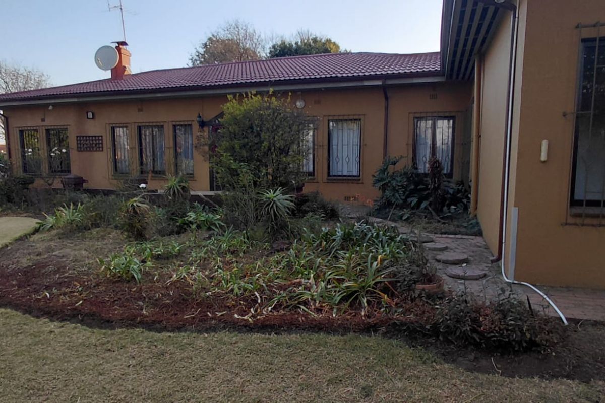 Rear view of the house featuring a tiled roof, brick facade, security bars on windows, and a paved walkway leading through the garden.