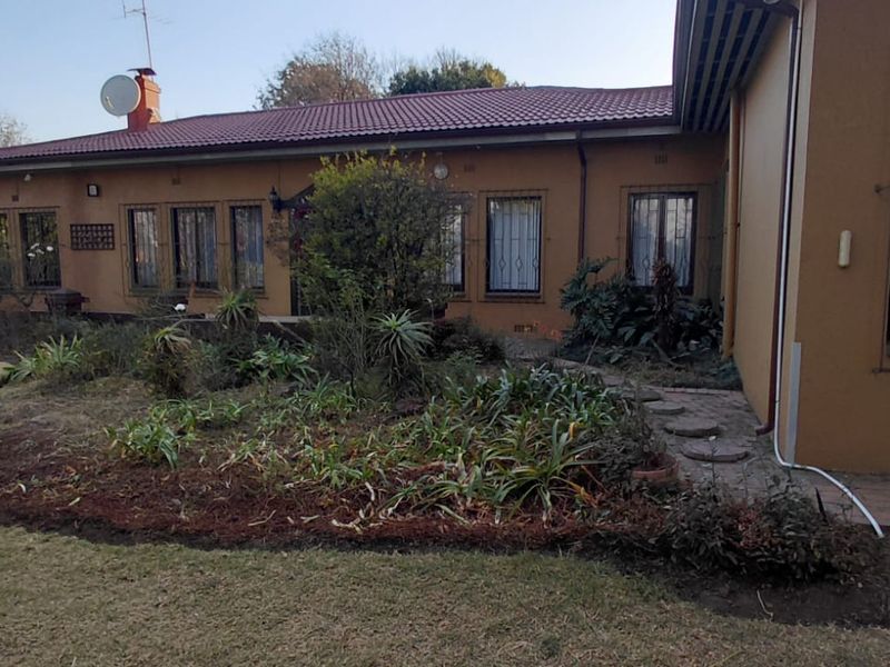 Rear view of the house featuring a tiled roof, brick facade, security bars on windows, and a paved walkway leading through the garden.