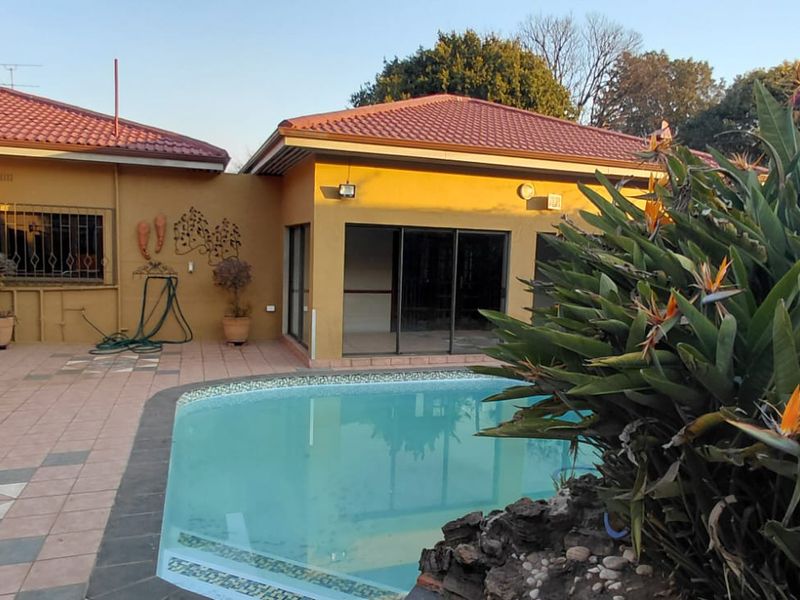 A rear exterior view featuring a swimming pool, tiled patio area, and access to the home through sliding glass doors.