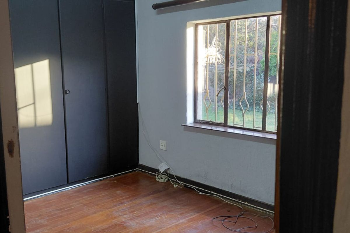 A vacant bedroom featuring timber flooring, built-in cupboards, and a window fitted with security bars.