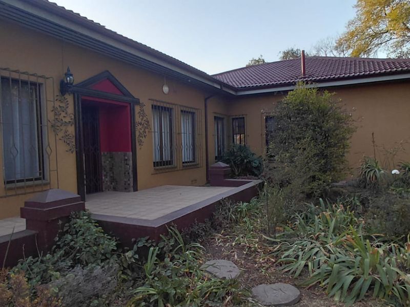 Front elevation of a single-story house featuring a tiled patio entrance, security bars on windows, and a mature garden setting.
