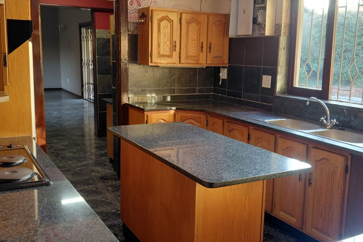 A functional kitchen featuring wooden cabinetry, granite countertops, a central island, and an integrated electric hob with a tiled backsplash.