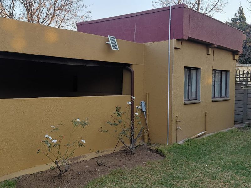 Rear view of the property featuring a covered patio area, solar lighting, and a small garden with a precast boundary wall.